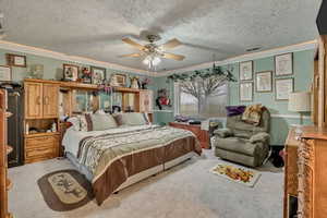 Bedroom featuring ornamental molding, light carpet, a ceiling fan, and a textured ceiling