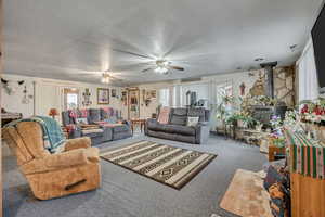 Carpeted living area featuring a wood stove, healthy amount of natural light, and a ceiling fan