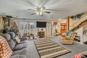 Living area featuring a wood stove, light carpet, and ceiling fan