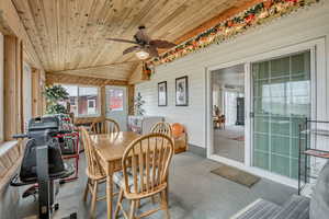 Dining room with a ceiling fan, a vaulted wood ceiling, carpet flooring, healthy amount of natural light, and wood walls