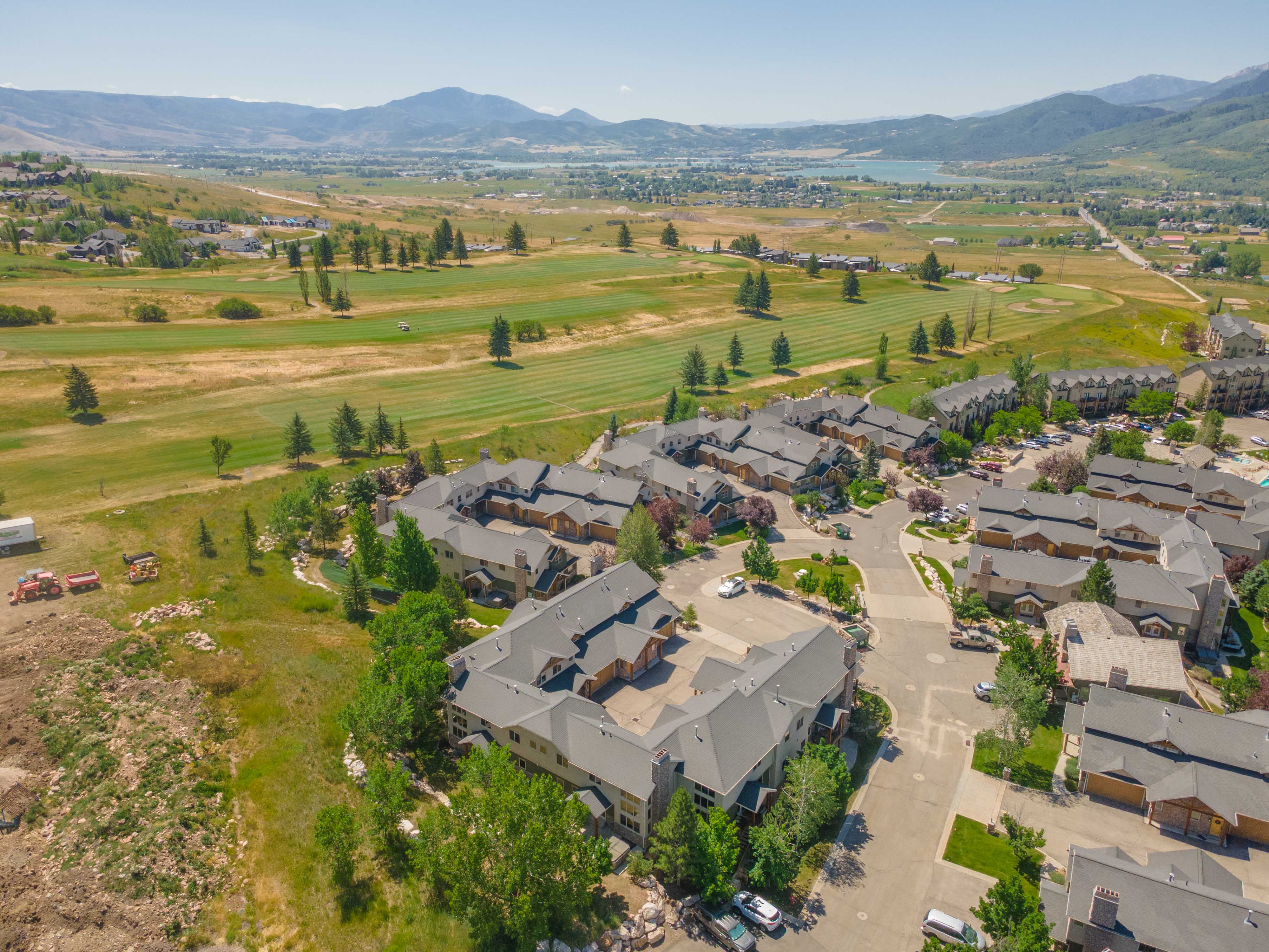 Aerial perspective showcasing a community of multi-story buildings, golf course frontage, surrounding mountains, a distant body of water, and mature landscaping