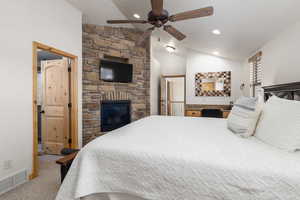 Bedroom featuring a stone fireplace, light carpet, and a ceiling fan