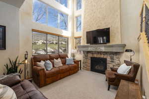 Living area with a high ceiling, a stone fireplace, and carpet flooring
