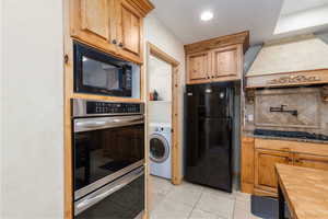 Kitchen featuring black appliances, backsplash, washer / clothes dryer, butcher block counters, and light tile patterned flooring