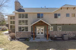 View of front facade with stone siding, a shingled roof, french doors, a chimney, and stucco siding