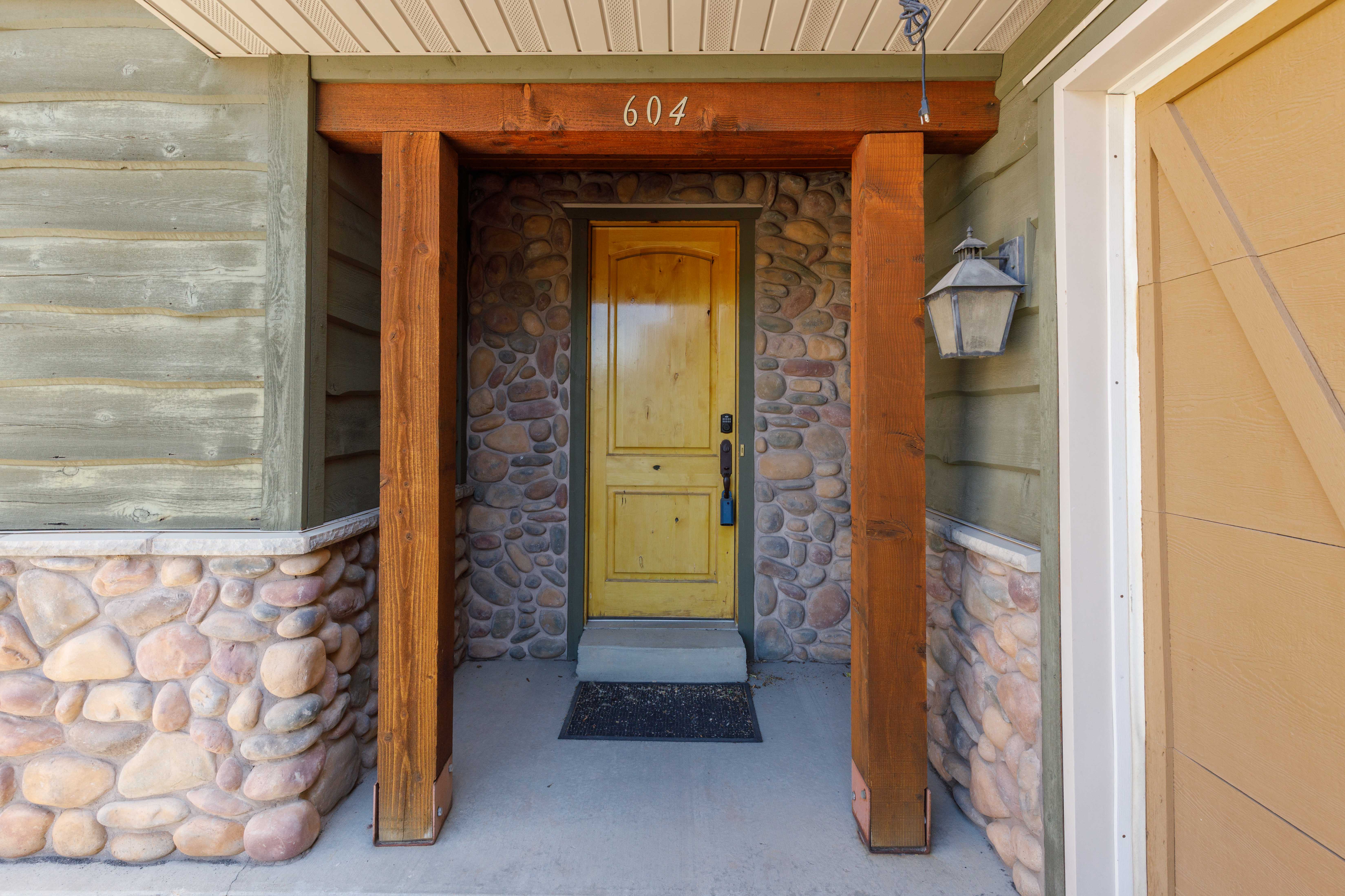 Entryway featuring a wood-panel door, stone wall accents, wood support beams, and horizontal siding