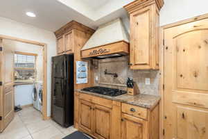 Kitchen featuring light stone counters, washing machine and clothes dryer, black appliances, tasteful backsplash, and light tile patterned floors