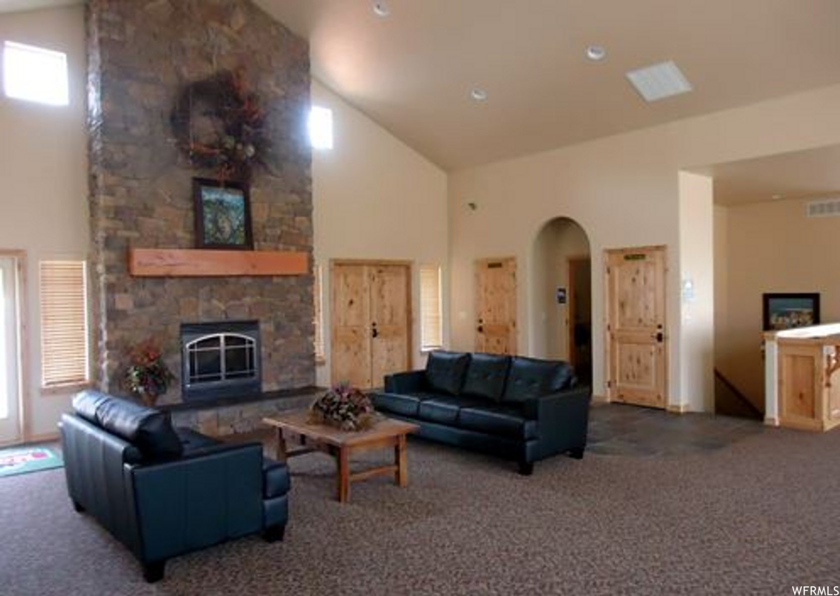 Living area with a stone fireplace, arched walkways, lofted ceiling, and carpet floors