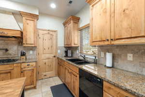 Kitchen featuring black appliances, light stone counters, light tile patterned floors, and decorative backsplash
