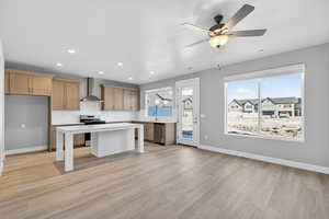Kitchen featuring stainless steel appliances, a kitchen island, a ceiling fan, light wood-style flooring, and a kitchen bar
