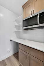 Kitchen view of stainless steel microwave, light wood finished floors, light stone countertops, light wood finish cabinets, and decorative backsplash