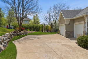 View of home's exterior with a lawn, a shingled roof, stone siding, driveway, and stucco siding