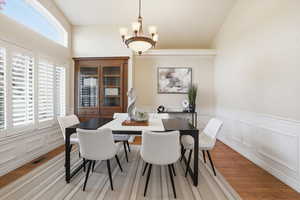 Dining area featuring a decorative wall, light wood-style floors, suspended lighting, and a wainscoted wall