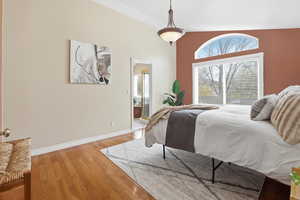Bedroom with light wood-style flooring, connected bathroom, and vaulted ceiling