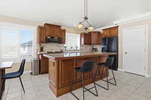 Kitchen with wood finish cabinets, a kitchen island, black appliances, a breakfast bar, and light tile patterned floors