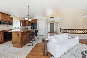 Kitchen featuring arched walkways, black appliances, wood finish cabinetry, a center island, and light countertops
