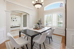 Dining room featuring a decorative wall, light wood-style floors, arched walkways, wainscoting, and ornate columns