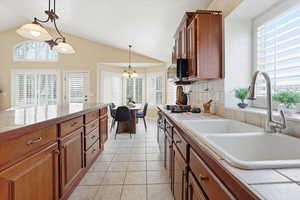 Kitchen with wood finish cabinetry, decorative light fixtures, plenty of natural light, light tile patterned flooring, and vaulted ceiling