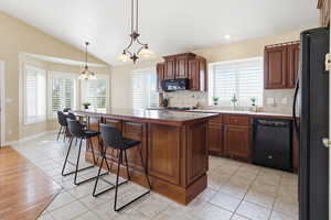 Kitchen with light tile patterned flooring, black appliances, a kitchen island, a breakfast bar area, and tasteful backsplash