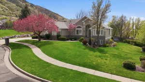View of front of property featuring a front yard, stone siding, stucco siding, and a shingled roof