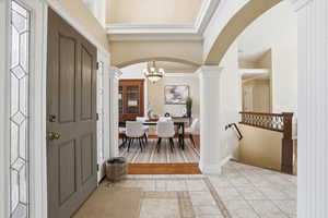 Foyer entrance with inlaid floor details, arched walkways, ornamental molding, light tile patterned flooring, and a chandelier