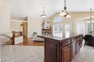 Kitchen featuring light tile patterned floors, open floor plan, hanging light fixtures, dark wood finish cabinets, and vaulted ceiling