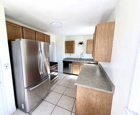 Kitchen with stainless steel appliances, light tile patterned floors, wood finish cabinetry, and light countertops
