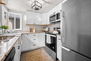 Kitchen with stainless steel appliances, light stone countertops, white cabinets, light wood-style flooring, and a textured ceiling