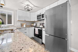 Kitchen with stainless steel appliances, white cabinets, light stone counters, a textured ceiling, and light wood finished floors