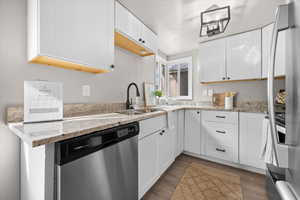 Kitchen featuring stainless steel appliances, white cabinets, light stone countertops, a textured ceiling, and light wood-type flooring