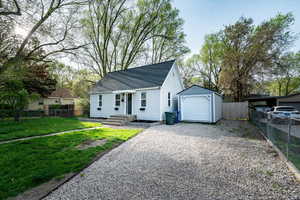 View of front of property featuring a shingled roof, gravel driveway, a garage, and an outdoor structure
