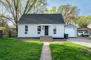 New england style home featuring a shingled roof, a detached garage, a front lawn, an outdoor structure, and gravel driveway