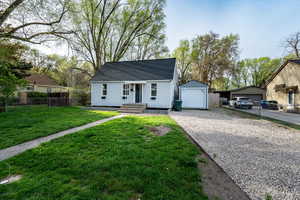 View of front facade with a garage, roof with shingles, driveway, and an outbuilding