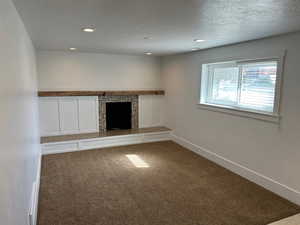 Unfurnished living room featuring dark colored carpet, a fireplace, recessed lighting, and a textured ceiling