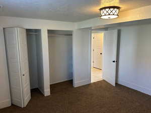 Unfurnished bedroom with a textured ceiling, multiple closets, and carpet flooring