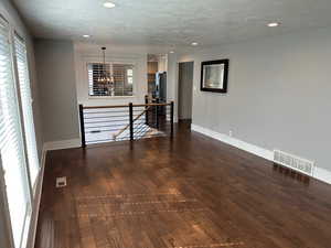 Empty room with dark wood finished floors, hanging lights, and a textured ceiling