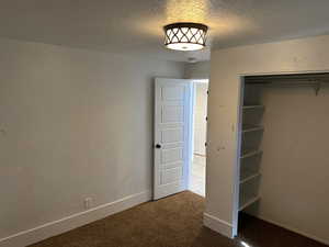 Unfurnished bedroom featuring a textured ceiling, dark carpet, and a closet