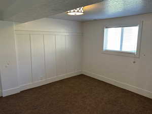 Spare room with dark carpet, a textured ceiling, a decorative wall, and wainscoting