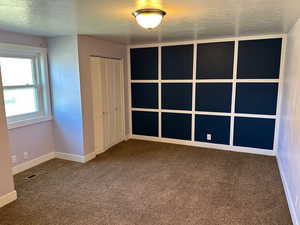 Unfurnished bedroom with a textured ceiling, dark carpet, and a closet