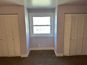 Unfurnished bedroom with multiple closets, dark colored carpet, and a textured ceiling