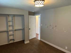 Unfurnished bedroom with dark carpet, a closet, and a textured ceiling
