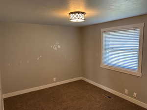 Empty room featuring dark carpet and a textured ceiling