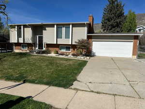 Bi-level home featuring brick siding, concrete driveway, an attached garage, and a chimney