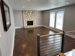 Unfurnished living room with a fireplace, dark wood-type flooring, a textured ceiling, and recessed lighting