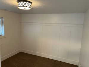 Spare room featuring a textured ceiling, dark carpet, a decorative wall, and a wainscoted wall