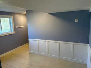 Hallway with a textured ceiling, a decorative wall, and wainscoting