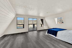 Bedroom with wooden walls, dark wood finished floors, access to outside, and a textured ceiling