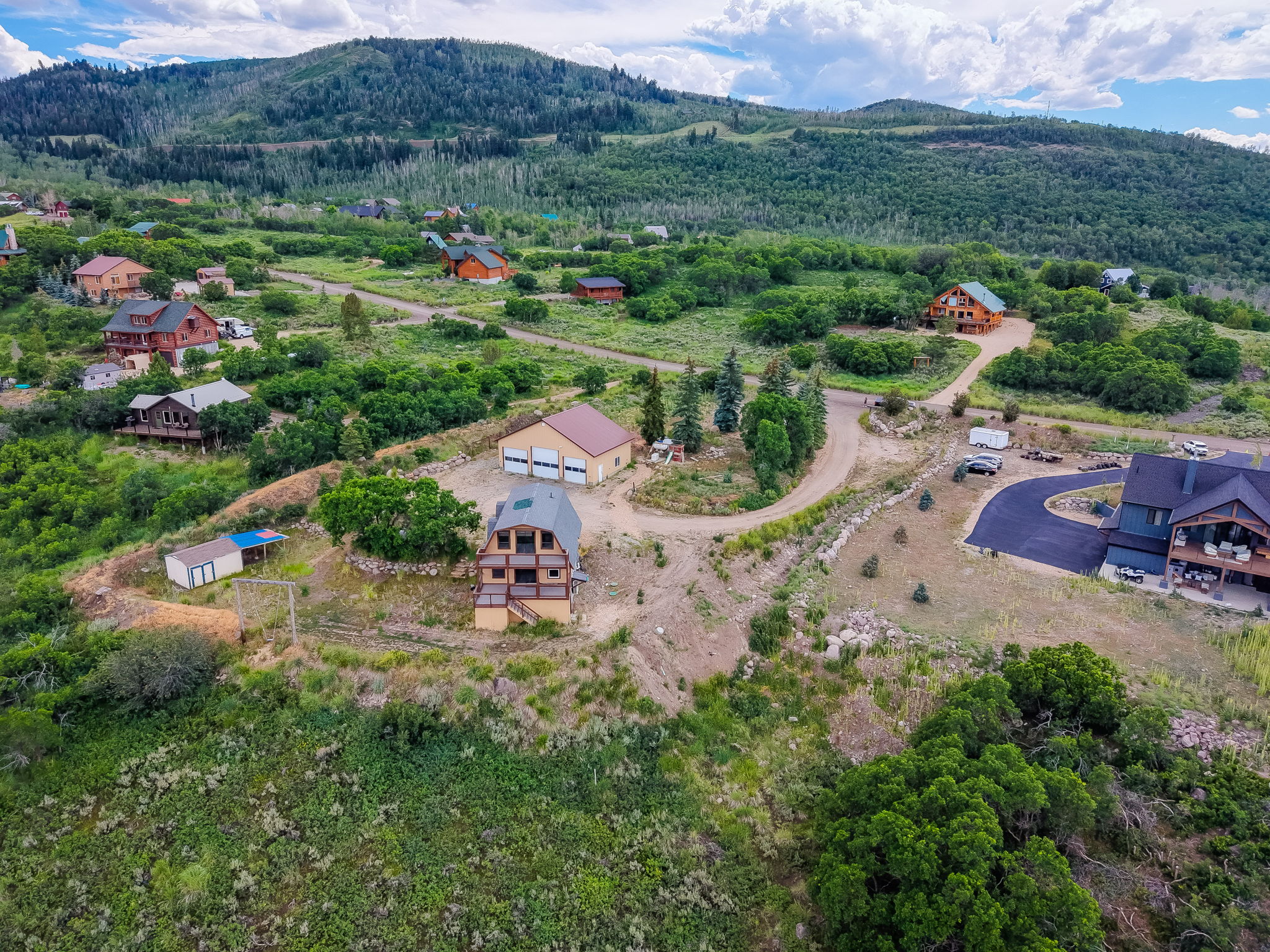 Expansive hillside property featuring multiple structures including a two-story residence with tiered balconies, a large detached garage with two bay doors, and an additional storage shed