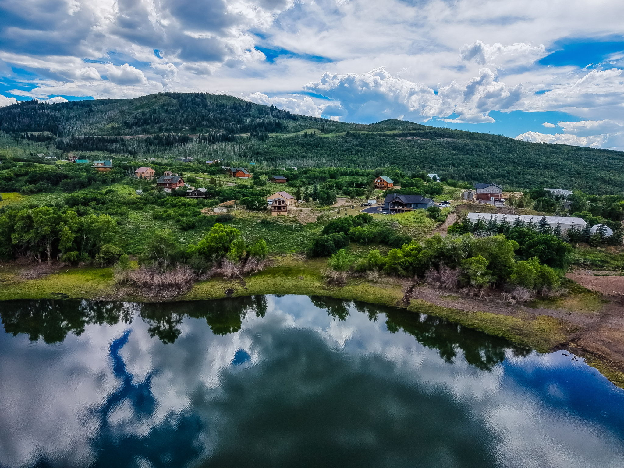 Mountain landscape with a body of water reflecting the sky, surrounded by lush green foliage and scattered residences