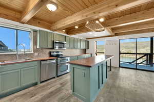 Kitchen with green cabinets, wood counters, stainless steel appliances, backsplash, and a wooden ceiling with exposed beams